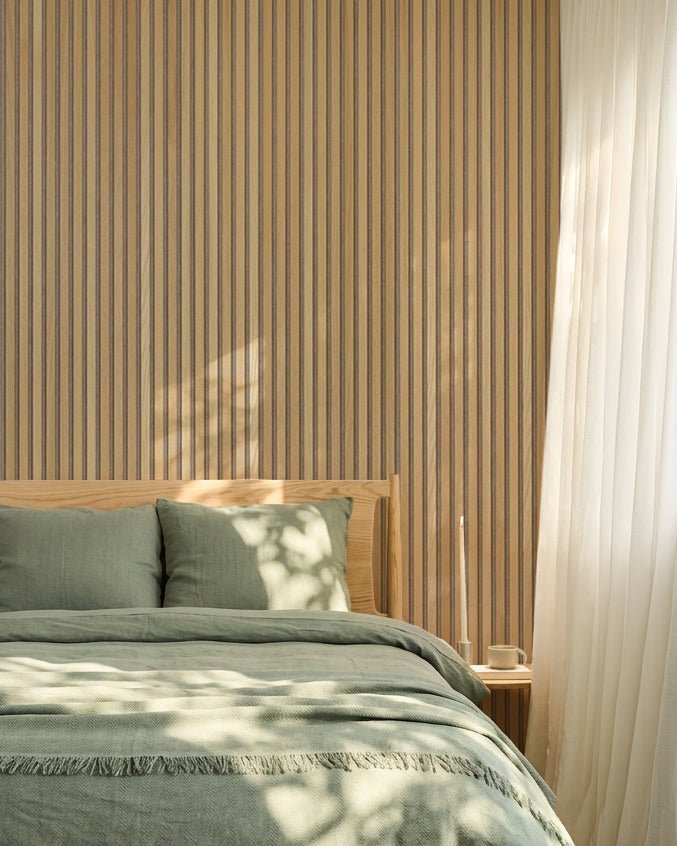Minimalist Nordic bedroom featuring a WoodUpp Akupanel oak acoustic panel wall, sage green bedding, wood bed frame, and sheer white curtains.